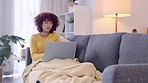 Woman typing an email and browsing online on a laptop while relaxing on the couch at home alone. Young and serious female entrepreneur or freelance worker brainstorming and planning business ideas