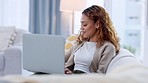Young woman answering the phone and surfing the internet with her laptop. Cheerful, trendy and edgy female relaxing on the sofa, chatting on a call and shopping online all from the comfort of home