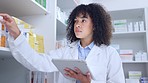 Pharmacist doing inventory with a digital tablet in a pharmacy. Young chemist with afro using pharma app to do stock update while counting and recording the quantity of medication in a drugstore 
