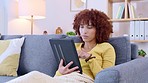 Woman browsing blogs, scrolling social media and streaming series online to enjoy on the weekend. Young female searching on a digital tablet while shopping online and relaxing on a sofa at home