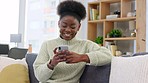 Woman typing a text message and scrolling on social media while relaxing on couch in the lounge at home. One young, carefree, and happy black female browsing the internet and chatting with friends