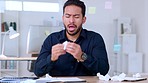 Sick business man sneezing and blowing his runny nose with a tissue while working in an office. Guy feeling unwell with flu, cold and covid symptoms while congested with sinuses and spring allergies

