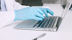 Hands of a scientist in surgical gloves, typing on a laptop in a medical lab. Closeup of a healthcare professional studying, making discovery and innovative breakthrough through DNA and RNA research