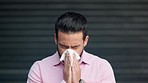 Young sick man in background blowing nose in tissue. Male having an allergic reaction in of medicines for treatment. Isolated guy over black background sneezing into disposable paper towel.