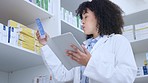 Pharmacist doing inventory with a digital tablet in a pharmacy. Young chemist with afro using pharma app to do stock update while counting and recording the quantity of medication in a drugstore