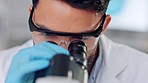 Research, examination and inspection being done by a doctor in a lab with a microscope. Young and serious medical researcher looking closely at a discovery while working to find a cure for disease