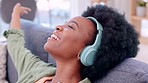 Happy, smiling and cheerful woman listening to music while singing, dancing and having fun in the lounge at home. Carefree, joyful and relaxed female in a good mood enjoying songs with headphones
