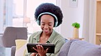 Happy, smiling and African woman browsing, streaming and watching videos online on a tablet with headphones at home. Cheerful, joyful, and relaxed black female enjoying music while searching the web