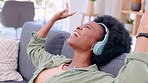 Happy, carefree and relaxed woman listening to music on headphones while sitting on a sofa in her living room at home. Happy female dancing and smiling while streaming playlist songs over the weekend