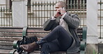 Trendy, stylish businessman on a phone call checking time, schedule or making business appointment and looking busy outdoors on a bench. A corporate professional man talking on a cellphone in a park