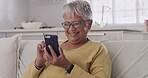 Senior latin woman on phone, relaxing, sitting on couch and laughing. Female texting, browsing social media online and watching funny, comedy videos while relaxing in the living room