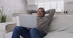 Happy, smiling elderly man enjoying entertainment on laptop while relaxing on sofa at home. Mature and retired male loving his fast internet, good wifi and high speed connection, streaming service.
