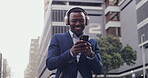 Happy businessman listening to music on his phone and wireless headphones while dancing. Smiling, joyful and professional male celebrating receiving a promotion. Cheerful guy browsing on technology.