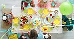Birthday party, balloons and cake for children celebrating together at a rainbow decorated table from above. Summer fruits and sweet treats being served while kids have fun