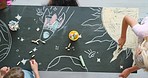Group of creative little boys and girls drawing a picture of outer space in a preschool classroom from a top view. A young class of kindergarten kids, students or learners doing an artwork