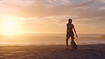 A female playing with her dog, throwing a ball at the beach during sunrise with copyspace. Young woman enjoying her day relaxing at the sea with her pet animal at sunrise in the morning