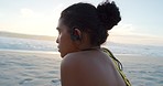 Fit, sporty and active female removing her earphones after a workout at the beach. Tired and exhausted woman resting and taking a break after exercise with waves in the sunset background