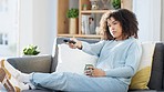 Black woman watching tv, having coffee and choosing what to watch while sitting on the sofa at home. African American woman finding funny movie, laughing, enjoying indoor entertainment on the weekend