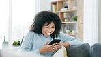 Woman smiling holding a phone and reading a loving text message, email or social media post while sitting on the couch at home. One happy, excited and smiling black female looking browsing the web