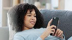 Closeup of smiling, relaxing female typing on a phone, chatting on social media while lounging on a sofa at home. Happy woman texting or replying to a funny message online while laying on a couch.