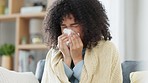 Sick young woman, with covid or cold at home on the sofa. Female blowing her nose on her living room couch and recovering her health. Lady covering herself with blanket, taking care of illness