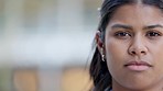 Young woman looking confident, serious and focused while standing outside against blurred background with copy space. Closeup face and head of a young female posing expressionless with copyspace