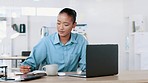 Female business worker working on a computer while drinking coffee at an office desk. Modern corporate worker typing an email while making finance notes. Smart young woman concentrating on work  
