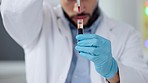 Closeup of scientist or doctor hands working on research with blood sample in test tube using medical equipment in lab. Focused male biologist analyzing red liquid substance vial, wearing gloves.