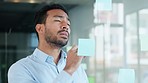 Professional man brainstorming and planning, thinking of marketing ideas while writing on sticky notes at work. Focused male making a visual board while researching a strategy and managing his tasks