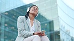 Trendy businesswoman with headphones listening to music on her phone during her work break outdoors. Young corporate woman enjoying songs on her stylish head wear against a modern building copy space