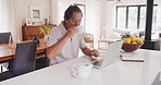 Old, mature and senior Asian male business executive working remote on a laptop in his modern house. An elderly, corporate and Chinese or Japanese man typing on a computer and drinking hot coffee