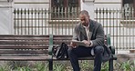 Handsome businessman browsing a tablet outside on a park bench. Serious and male scrolling on a social media app while relaxing alone in a park. Trendy young professional guy checking emails online