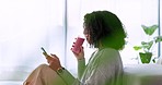 Social media, phone and smoothie woman in her living room reading a funny text. Smile, relax and happy black girl online on mobile with health fruit drink in hand for healthy lifestyle at house.
