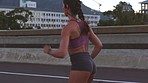 Woman running, exercise and fitness during a city workout for health and wellness while listening to music with wireless earphones. Fast and athletic woman training for a fit body on an urban bridge