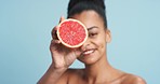 Grapefruit, black woman skincare and face skin with fruit for wellness, health and facial on a blue background in studio. Happy portrait, smile or beauty model with food product in hand for vitamin c