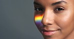 Face, beauty and rainbow with a woman model on a gray background in studio with mockup. Skin, care and makeup with a beautiful young female in the lgbt and gay community posing with a confident smile