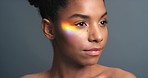 Rainbow, prism and light on face of black woman for glow, beauty or LGBT pride against a grey background in studio. Holographic, flare and reflection on young female for art, creative or skincare