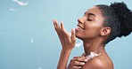 Beautiful black woman with soft skin taking feathers and touching her body in a studio. Happy, sensual African girl with a wellness lifestyle doing a luxury selfcare routine with blue background.