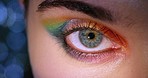 Female eyes with rainbow festival makeup, intense bright colors on eyelid and detail blue green pupil and iris. Closeup shows microblading on eyebrow, healthy and gold skin tone with a beautiful glow