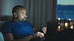 Tired man working at night time with laptop, while its dark outside, done working to close computer. African American guy in bed work online, close mobile pc after check watch and see sun has set