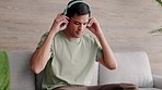 Young man, music headphones and phone social media apps, podcast and audio ebook listening on sofa at home. Relax, internet and mobile radio streaming, typing and online technology living room couch