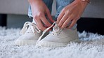 Fashion shoes, feet and woman hands with cool sneakers, trendy trainers or stylish footwear in house living room or home interior. Zoom on person opening shoe tie on relax lounge sofa or floor carpet