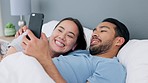 Happy interracial couple, bed and phone scroll of a Asian woman and Arab man in a bedroom. In love people at home relax at home looking at mobile internet, web and social media app content at a house