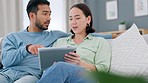 Asian couple, tablet and talking while doing online shopping, research or browsing social media to relax on couch at home. Enjoying internet entertainment with mobile app during weekend or free time