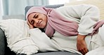 Woman, menstruation and pain on sofa in home living room with nausea and bloated tummy trouble. Stress, ache and stomach problem for arab girl with cramps from natural  period discomfort.