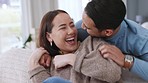 Love, happiness and fun with asian couple being playful and affectionate while laughing and tickling on the sofa at home. Happy man and woman bonding and joking together in a healthy relationship