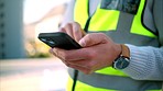 Construction worker texting on a phone, standing outdoors at a building site. Closeup of an architect or engineer checking a design development or online model, communication for design approval