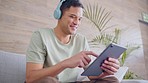 Headphones, tablet and a happy man watching online movies or videos on sofa at home. Entertainment, social media scrolling or motivation podcast on internet music streaming app with 5g wifi network