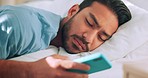 Wake up, tired and text with man in bed looking at phone messages, social media or internet app. Sleep, online and exhausted with young guy focus on screen while lying in bedroom at home