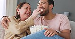 Popcorn, eating and love with a couple laughing on a sofa in the living room of their home. Food, joke and relax with a young man and woman sitting on a coach together in their house on the weekend